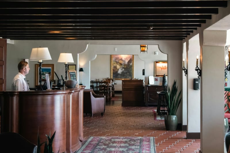 Empfangsbereich eines Hotels mit Mitarbeiter hinter dem Rezeptionstresen – Sinnbild für Gastfreundschaft und Forderungsmanagement in der Hotellerie.