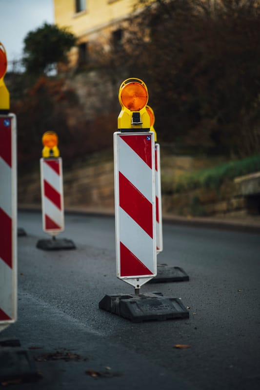 Rot-weiße Absperrbaken mit orangen Warnleuchten an einer Baustelle – Sinnbild für Frühwarnsignale in der Bau-Lieferkette.